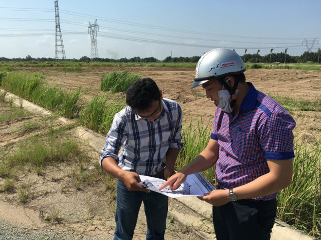 2 người đàn ông đang đứng xem 1 tấm bản đồ, xung quanh là khu đất rộng bỏ hoang