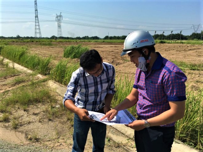 hai người đàn ông trẻ đứng xem bản đồ giữa một khu đất rộng lớn